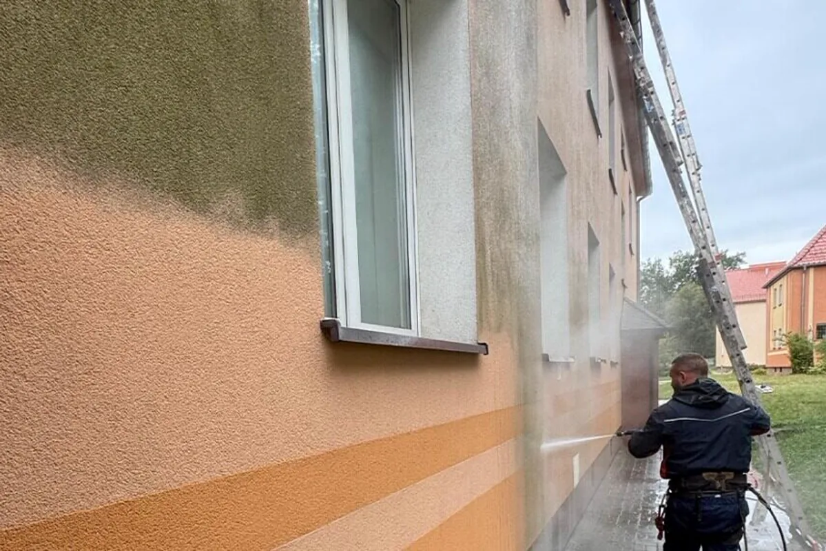 Renoskam-Fachkraft reinigt eine Putzfassade – links bereits sauber, rechts noch verschmutzt